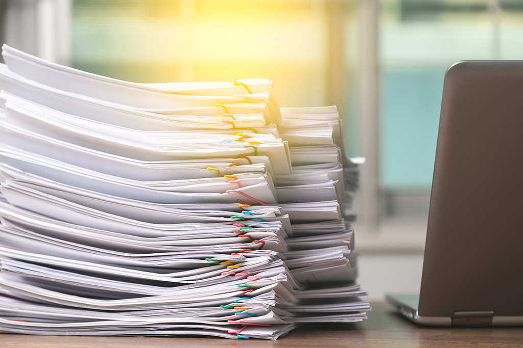 A stack of papers secured with paperclips on a table next to a laptop.