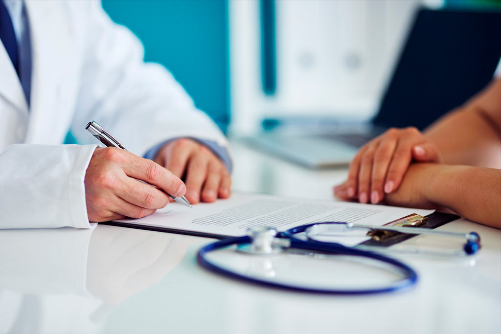 Doctor writing on a clipboard next to a stethoscope and a patient with their hands folded.