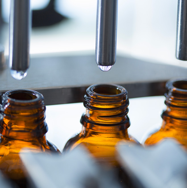 Two liquid droppers drip cannabis oil into identical glass bottles.